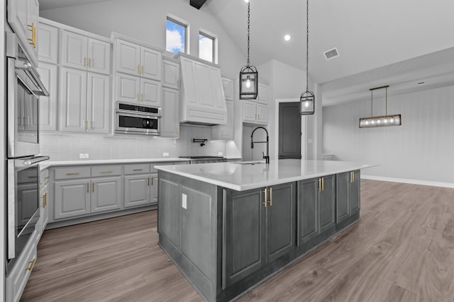 kitchen featuring decorative backsplash, a kitchen island with sink, sink, and light hardwood / wood-style flooring