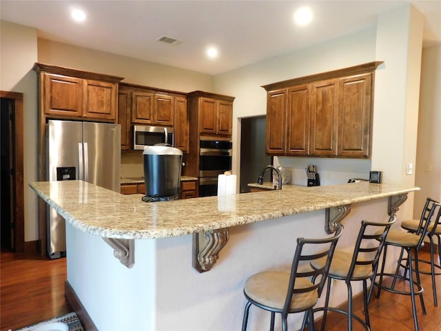 kitchen featuring kitchen peninsula, dark hardwood / wood-style flooring, light stone countertops, stainless steel appliances, and a kitchen bar