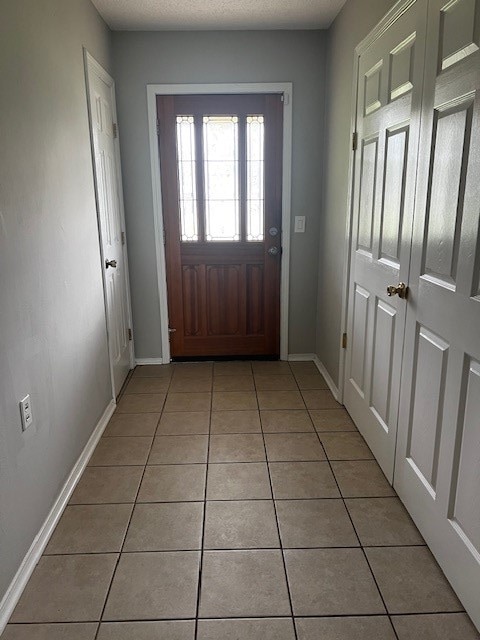 doorway with a textured ceiling and light tile patterned floors