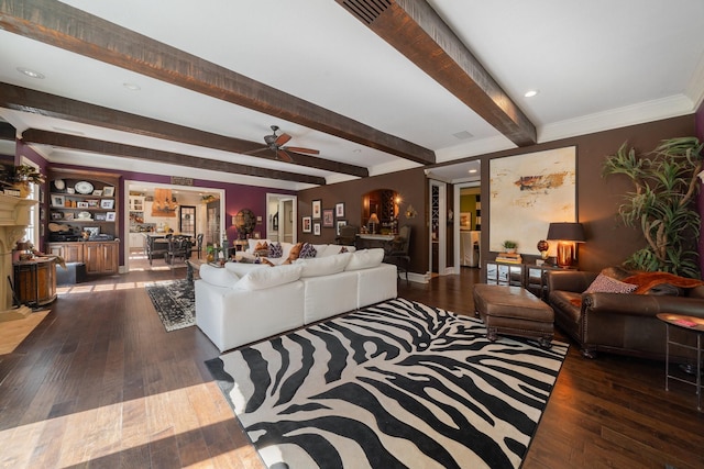 living room with dark wood-type flooring, ceiling fan, ornamental molding, a fireplace, and beamed ceiling