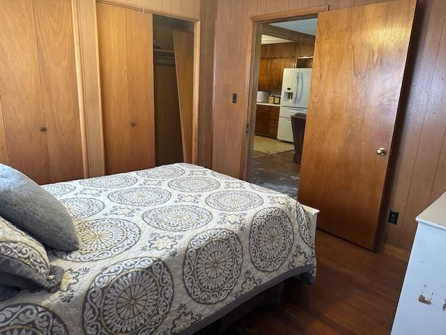 bedroom with wooden walls, wood finished floors, and white fridge with ice dispenser