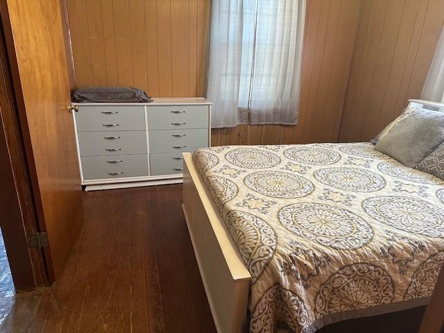 bedroom with dark wood-type flooring and wooden walls