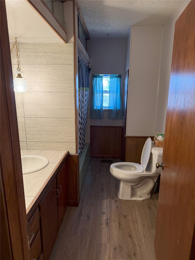 full bath featuring curtained shower, toilet, vanity, wood finished floors, and a textured ceiling