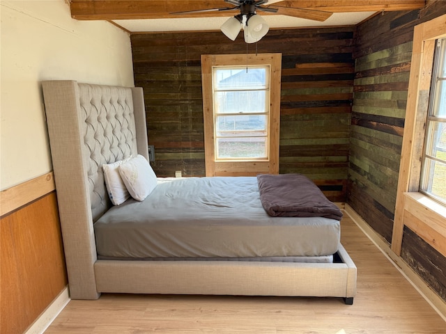 bedroom with light wood finished floors, wooden walls, multiple windows, and beamed ceiling