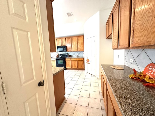 kitchen with light tile patterned floors, backsplash, dark stone counters, and black appliances