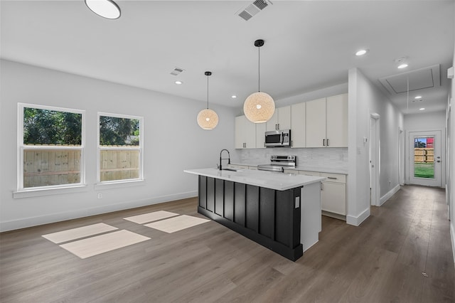 kitchen featuring hanging light fixtures, an island with sink, white cabinets, stainless steel appliances, and hardwood / wood-style floors