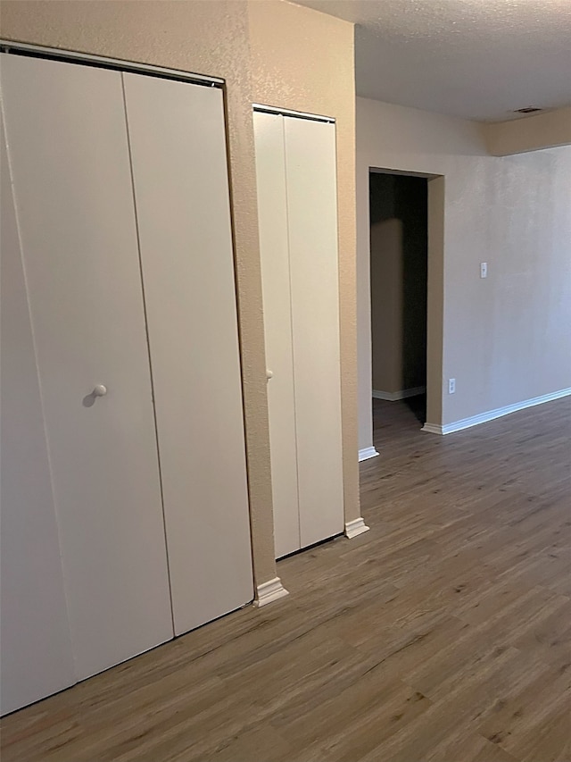 unfurnished bedroom featuring multiple closets, light hardwood / wood-style floors, and a textured ceiling