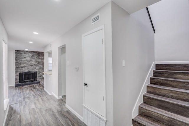 staircase with visible vents, a stone fireplace, baseboards, and wood finished floors
