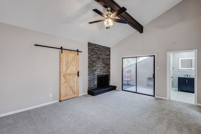 unfurnished living room with a barn door, a stone fireplace, beamed ceiling, ceiling fan, and light carpet