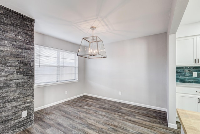 unfurnished dining area with a notable chandelier, dark wood-type flooring, and baseboards