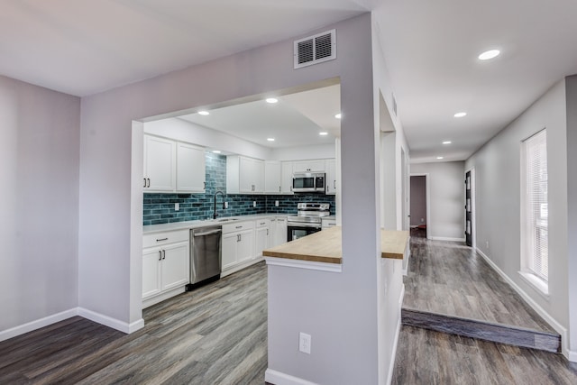 kitchen with appliances with stainless steel finishes, white cabinetry, tasteful backsplash, hardwood / wood-style flooring, and sink