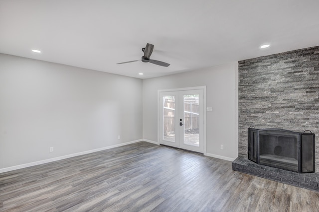 unfurnished living room with wood-type flooring, a stone fireplace, ceiling fan, and french doors