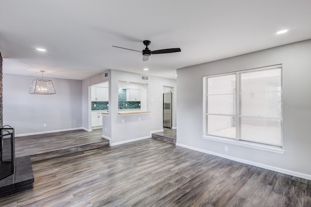 unfurnished living room with ceiling fan with notable chandelier and hardwood / wood-style floors