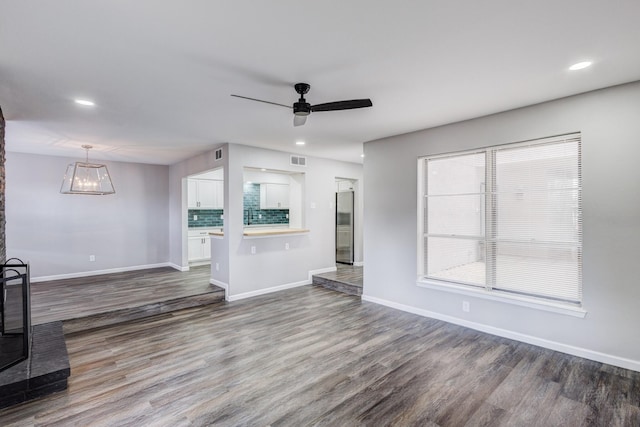 unfurnished living room featuring visible vents, ceiling fan with notable chandelier, baseboards, and wood finished floors