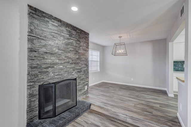 unfurnished living room featuring a notable chandelier, visible vents, baseboards, and wood finished floors
