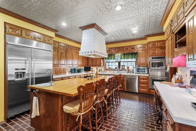 kitchen featuring ornamental molding, stainless steel appliances, butcher block countertops, and a kitchen island with sink