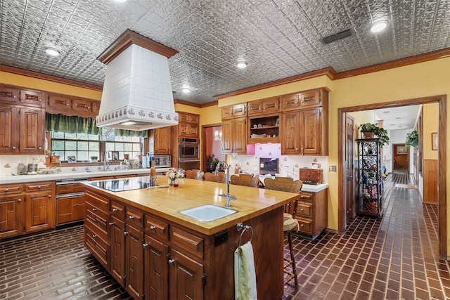 kitchen with black electric stovetop, sink, crown molding, a center island with sink, and wooden counters