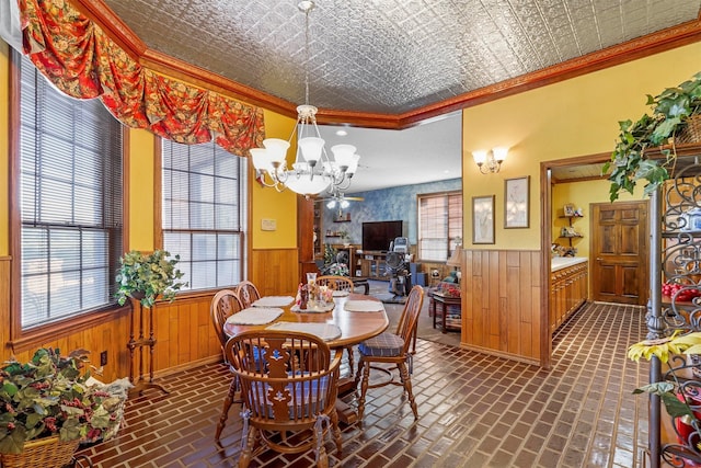 dining space with wood walls, ornamental molding, and a notable chandelier