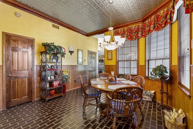 dining room featuring wood walls, ornamental molding, and an inviting chandelier