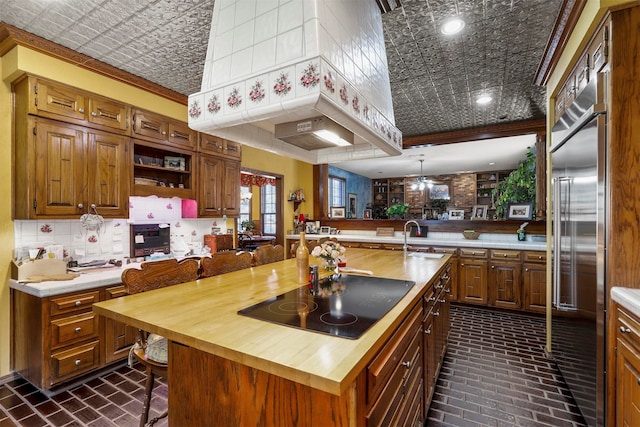 kitchen with black electric stovetop, kitchen peninsula, built in refrigerator, a center island with sink, and butcher block countertops