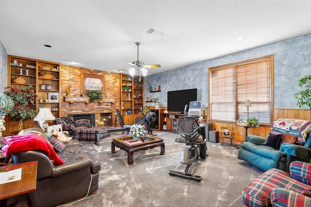 carpeted living room with built in features, ceiling fan, a fireplace, and a textured ceiling