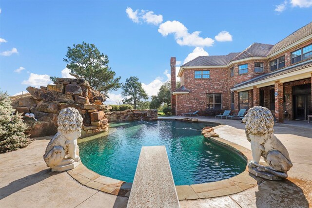 view of swimming pool featuring a diving board and a patio