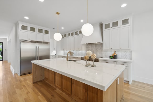 kitchen with white cabinetry, a kitchen island with sink, custom exhaust hood, and appliances with stainless steel finishes