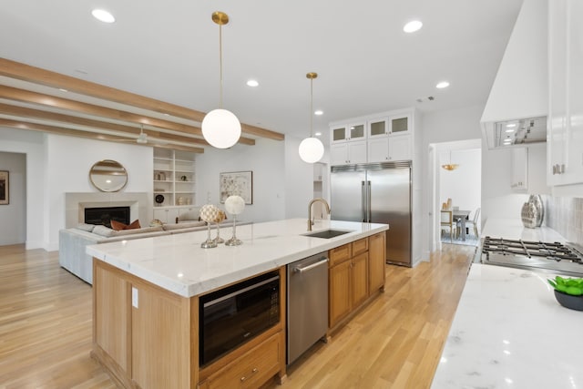 kitchen with light stone countertops, built in appliances, a center island with sink, white cabinets, and custom exhaust hood