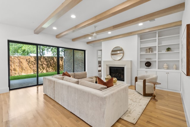 living room featuring beamed ceiling, built in shelves, light wood-type flooring, and ceiling fan