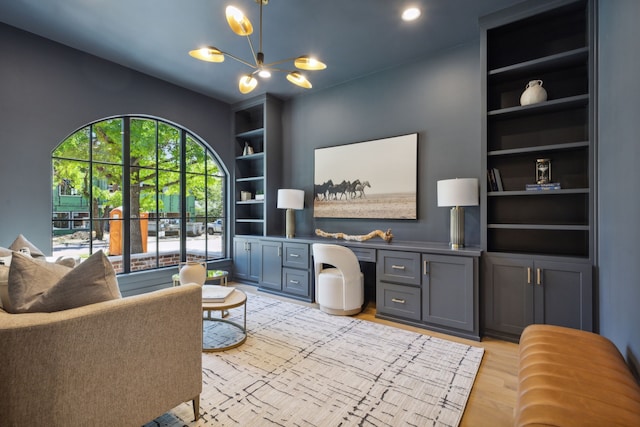 living room featuring light wood-type flooring, an inviting chandelier, built in shelves, and built in desk