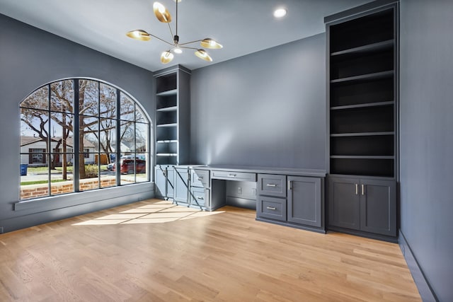 unfurnished office featuring a chandelier, built in shelves, built in desk, and light hardwood / wood-style flooring