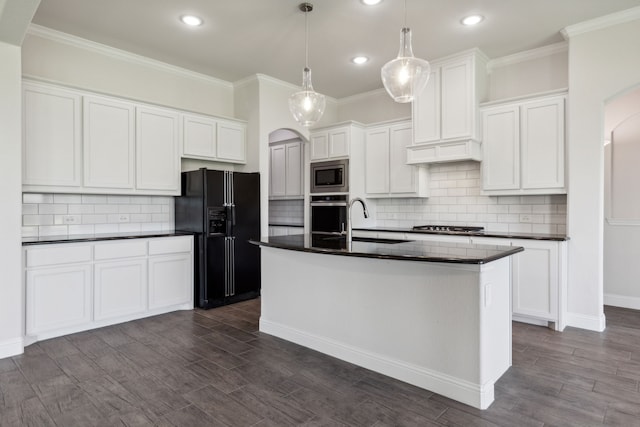 kitchen featuring white cabinets, dark countertops, an island with sink, appliances with stainless steel finishes, and hanging light fixtures