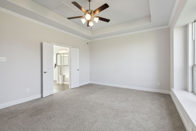 carpeted empty room with visible vents, baseboards, ceiling fan, ornamental molding, and a tray ceiling