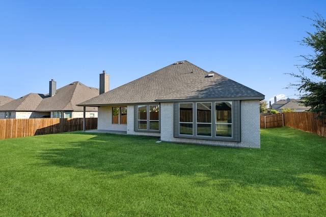 rear view of house with roof with shingles, brick siding, a lawn, and a fenced backyard