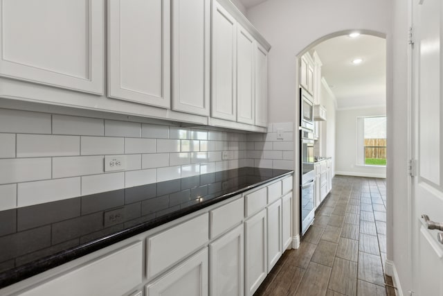 kitchen featuring dark countertops, arched walkways, white cabinets, and backsplash