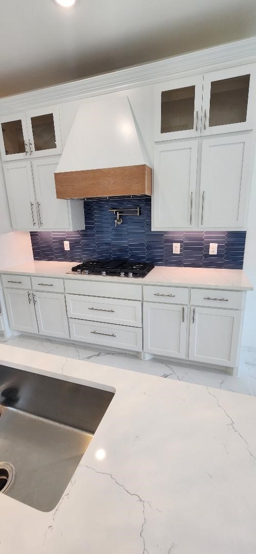 kitchen with stainless steel gas stovetop, white cabinets, custom range hood, and tasteful backsplash