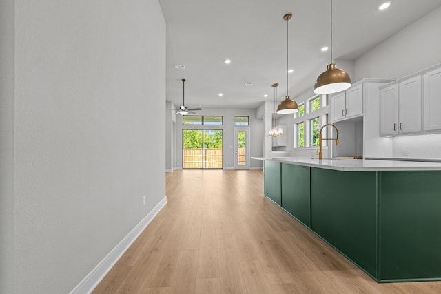 kitchen featuring white cabinetry, pendant lighting, light wood-type flooring, ceiling fan, and sink