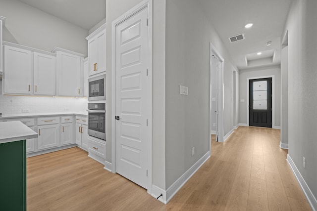 kitchen featuring white cabinets, backsplash, stainless steel oven, light hardwood / wood-style flooring, and built in microwave