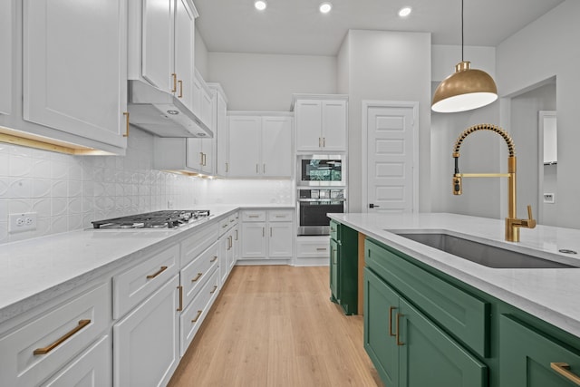 kitchen with hanging light fixtures, light hardwood / wood-style floors, white cabinetry, stainless steel appliances, and sink