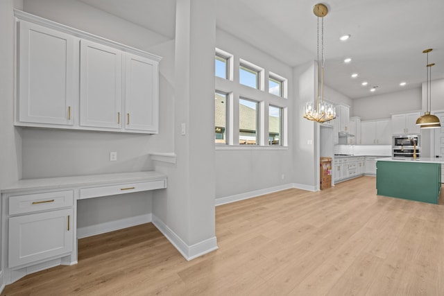 kitchen with built in desk, hanging light fixtures, white cabinetry, stainless steel appliances, and light wood-type flooring