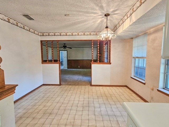 empty room featuring a textured ceiling and ceiling fan with notable chandelier