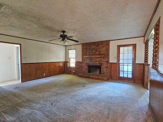 unfurnished living room featuring a textured ceiling, wood walls, light carpet, a brick fireplace, and ceiling fan