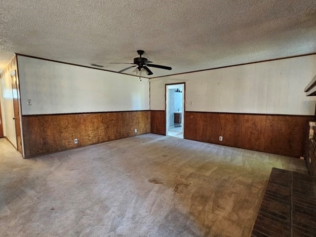 carpeted spare room featuring a textured ceiling, wood walls, and ceiling fan