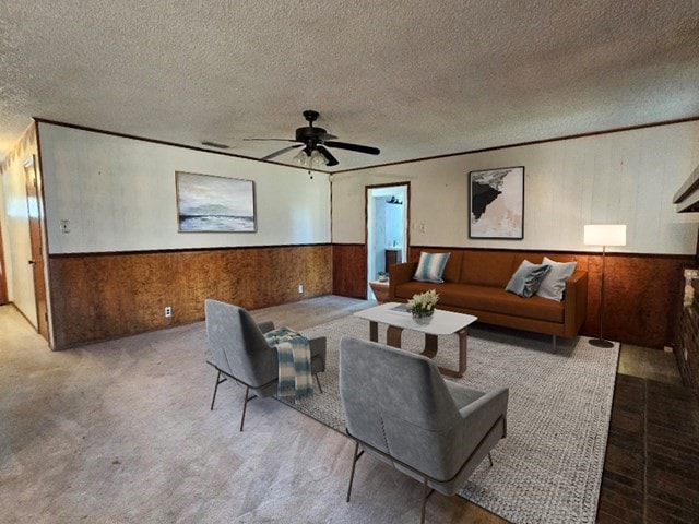 carpeted living room with ceiling fan, a textured ceiling, and wood walls