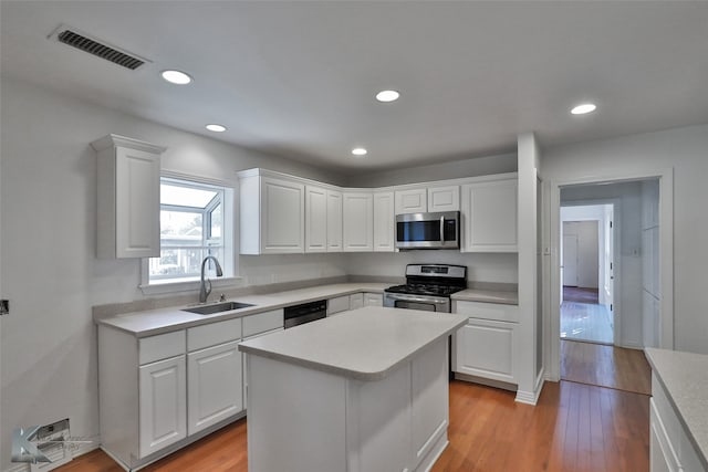 kitchen with a center island, sink, white cabinets, light hardwood / wood-style flooring, and appliances with stainless steel finishes