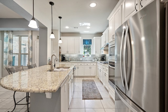 kitchen featuring white cabinetry, stainless steel appliances, a kitchen bar, a kitchen island with sink, and sink