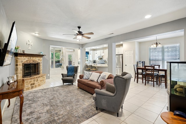 living room featuring ceiling fan with notable chandelier, a textured ceiling, a fireplace, and a healthy amount of sunlight