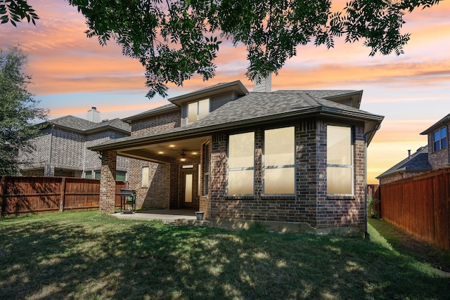 back house at dusk with a patio area and a yard