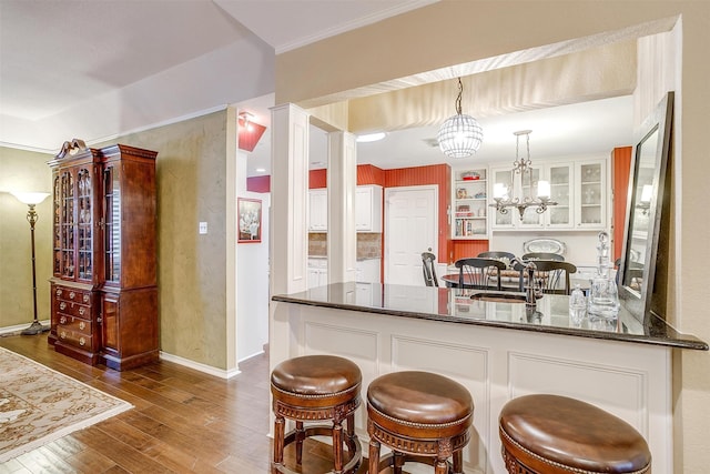 kitchen featuring dark hardwood / wood-style floors, a notable chandelier, kitchen peninsula, a kitchen bar, and decorative light fixtures