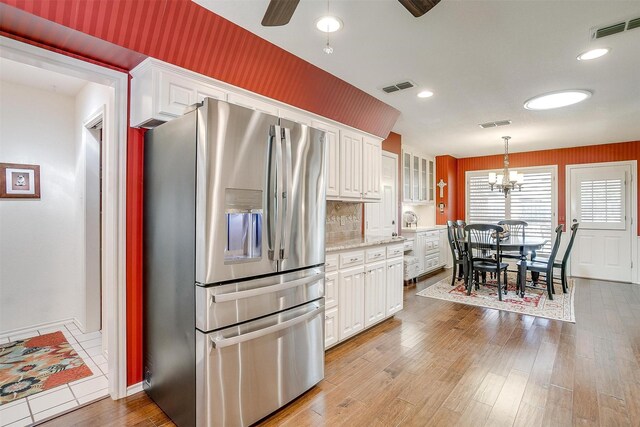 kitchen with light stone counters, light wood-type flooring, stainless steel fridge with ice dispenser, white cabinetry, and ceiling fan with notable chandelier